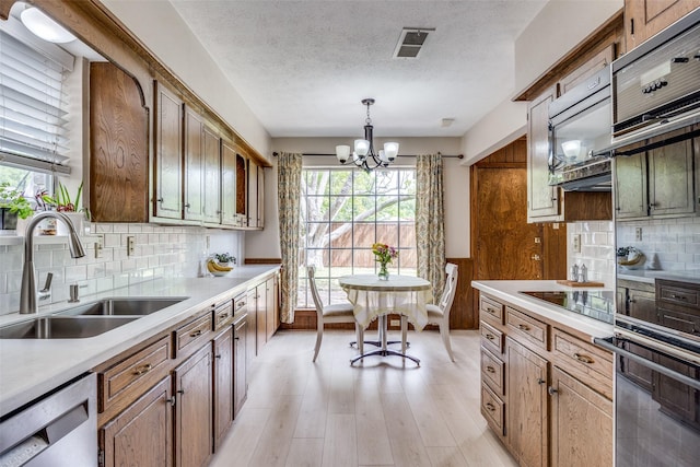 kitchen with a sink, visible vents, black appliances, light wood-type flooring, and a notable chandelier