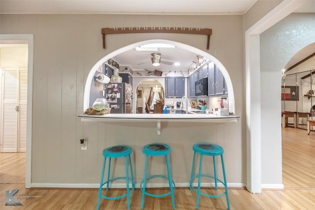 bar featuring freestanding refrigerator, black microwave, arched walkways, a ceiling fan, and wood finished floors