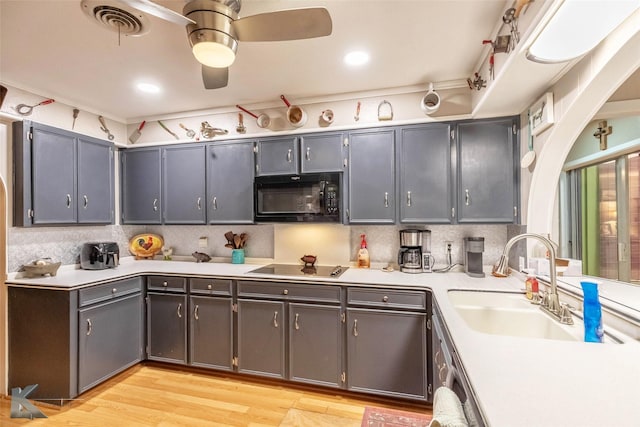 kitchen with a sink, light countertops, light wood-type flooring, black appliances, and backsplash