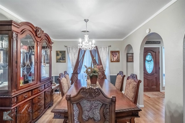 dining space with crown molding, light wood finished floors, arched walkways, and an inviting chandelier