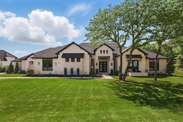 view of front of property featuring roof with shingles, french doors, a front lawn, and brick siding