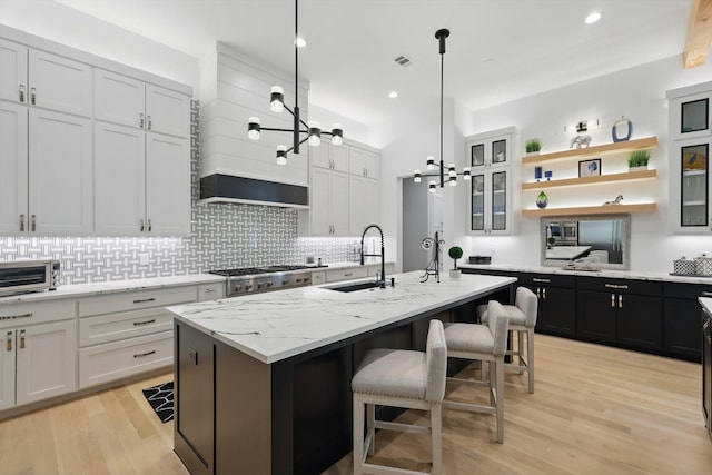 kitchen featuring white cabinets, a sink, light wood-style floors, a center island with sink, and decorative backsplash