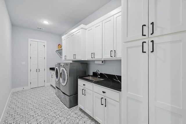 clothes washing area featuring separate washer and dryer, visible vents, a sink, baseboards, and cabinet space