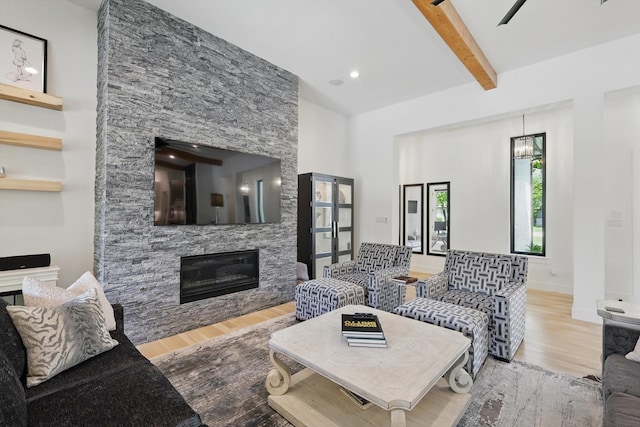 living area with beamed ceiling, a stone fireplace, recessed lighting, wood finished floors, and baseboards
