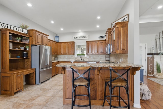 202 Hill Valley Dr, Stephenville, TX 76401 - kitchen featuring a peninsula, backsplash, brown cabinetry, appliances with stainless steel finishes, and a sink
