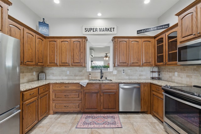 202 Hill Valley Dr, Stephenville, TX 76401 - kitchen with light stone counters, glass insert cabinets, brown cabinetry, appliances with stainless steel finishes, and a sink