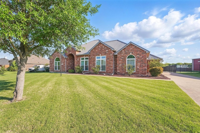 view of front of house with a front yard, brick siding, fence, and metal roof