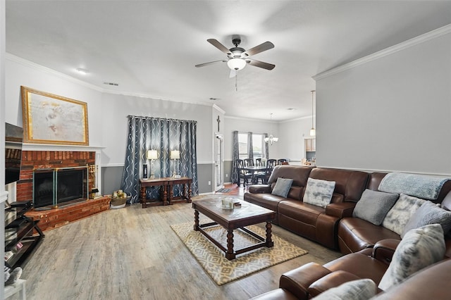 living room featuring visible vents, ornamental molding, a fireplace, wood finished floors, and ceiling fan with notable chandelier