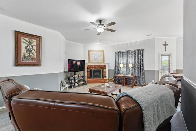 living area featuring crown molding, a brick fireplace, visible vents, ceiling fan, and wood finished floors