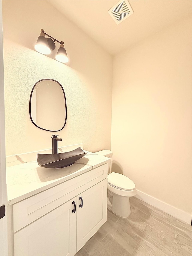 half bathroom with vanity, baseboards, toilet, visible vents, and wood finished floors