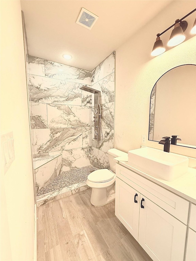 bathroom featuring visible vents, toilet, vanity, wood finished floors, and a stall shower