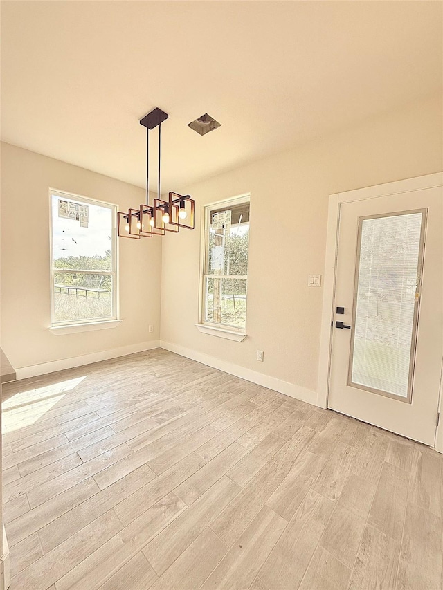 unfurnished dining area with baseboards, light wood finished floors, and a chandelier