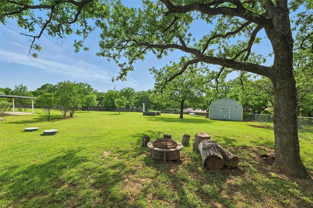 view of yard with fence, an outbuilding, a fire pit, and a storage shed