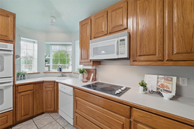 kitchen featuring a sink, brown cabinets, white appliances, and light countertops