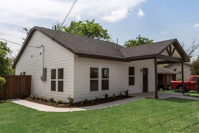 view of front facade with a shingled roof, a front yard, and fence