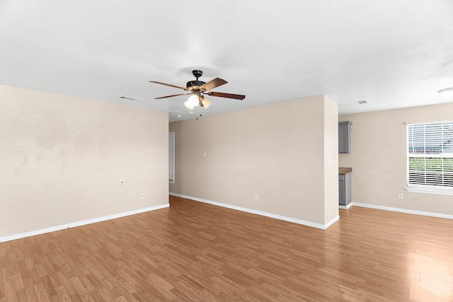 unfurnished room with light wood-style floors, visible vents, a ceiling fan, and baseboards