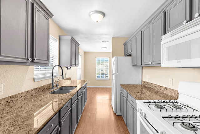 kitchen featuring light wood-style flooring, a sink, gray cabinetry, white appliances, and light stone counters