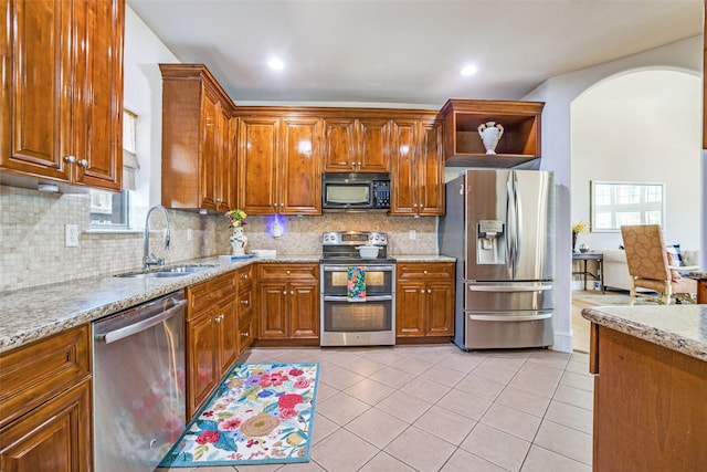 kitchen with light stone counters, a sink, appliances with stainless steel finishes, arched walkways, and light tile patterned flooring