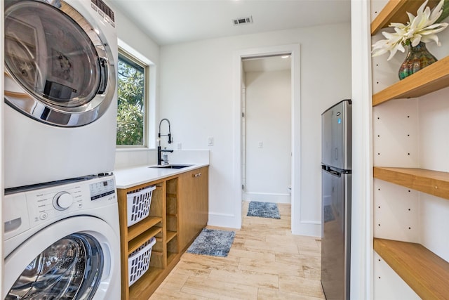 laundry room with visible vents, stacked washing maching and dryer, light wood-style floors, and a sink