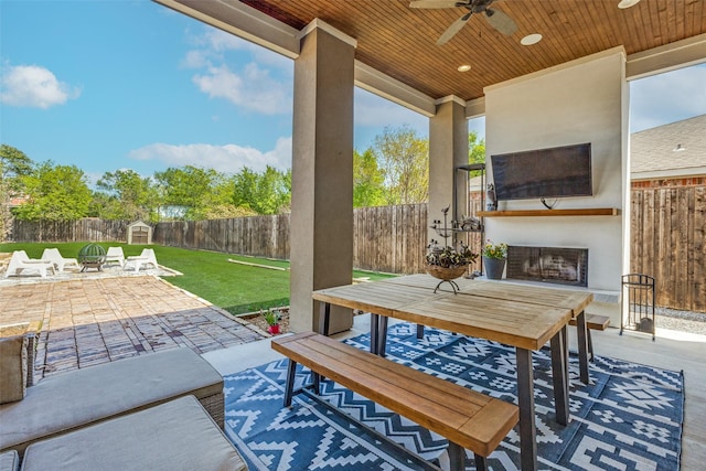 view of patio / terrace featuring outdoor dining area, a fenced backyard, an outdoor fireplace, a ceiling fan, and a storage unit