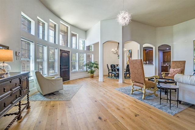 living room with a high ceiling, a chandelier, baseboards, arched walkways, and hardwood / wood-style flooring