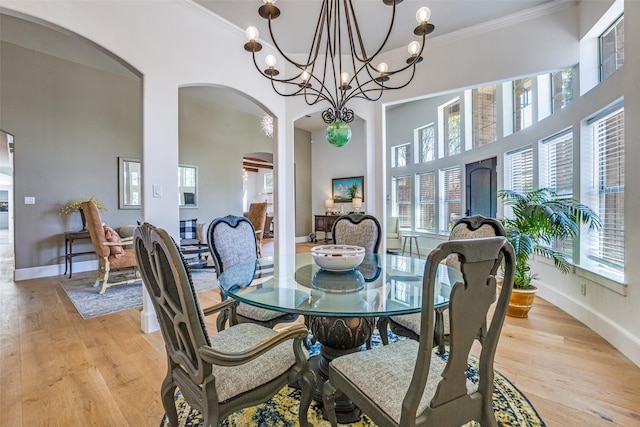 dining room featuring a high ceiling, a notable chandelier, crown molding, light wood-style flooring, and arched walkways