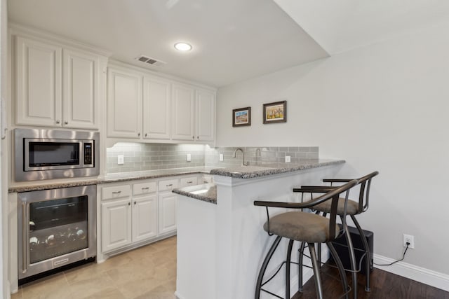 kitchen with wine cooler, a breakfast bar, visible vents, stainless steel microwave, and a peninsula