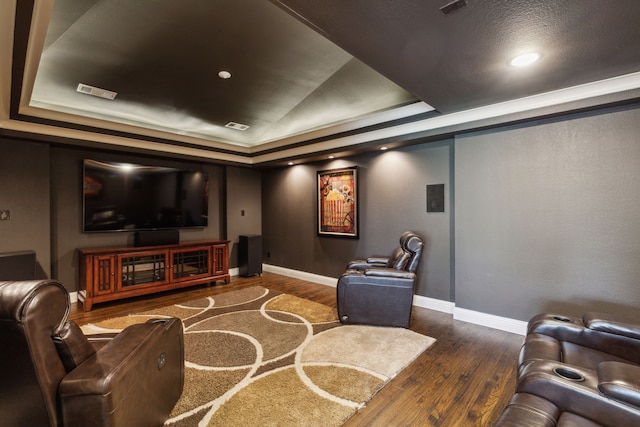 home theater room featuring baseboards, a tray ceiling, visible vents, and hardwood / wood-style floors