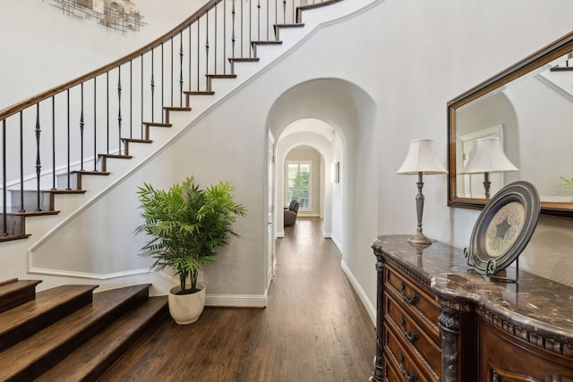 foyer featuring arched walkways, wood finished floors, baseboards, and stairway