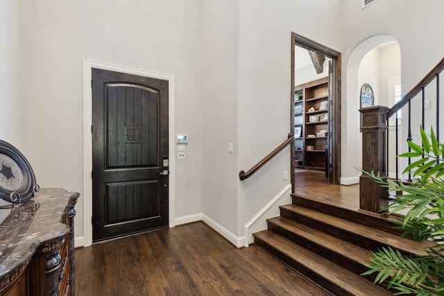 entrance foyer with stairs, a towering ceiling, arched walkways, and dark wood-type flooring