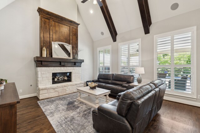 living room with beam ceiling, dark wood-style flooring, baseboards, ceiling fan, and a stone fireplace