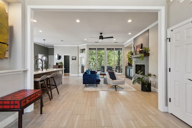 living area featuring baseboards, ceiling fan, a fireplace, crown molding, and recessed lighting