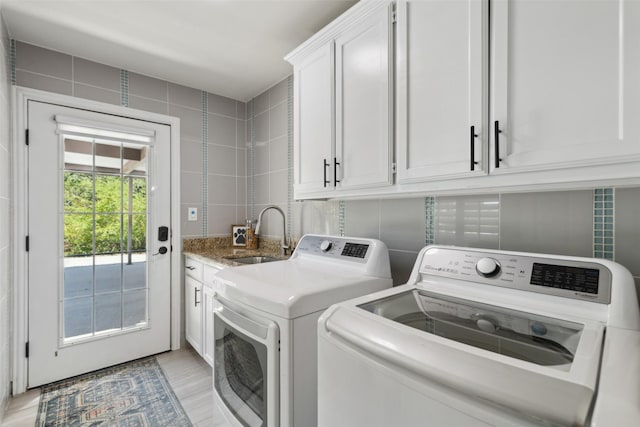 laundry room featuring a sink, tile walls, light wood-type flooring, cabinet space, and washing machine and dryer