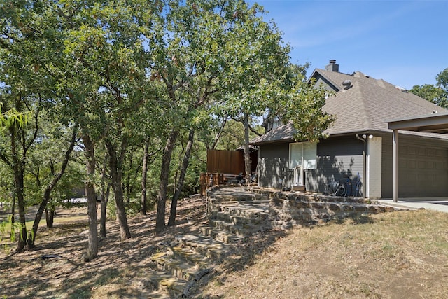 view of side of property featuring an attached garage and roof with shingles