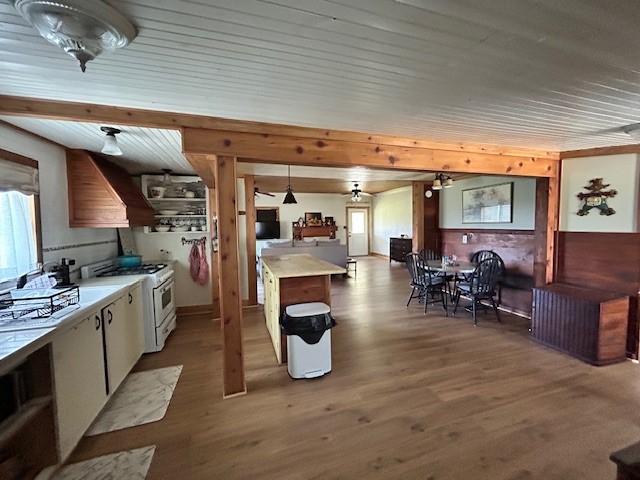 kitchen with custom exhaust hood, light wood-style flooring, light countertops, and white gas range