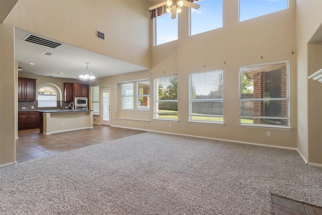 unfurnished living room featuring ceiling fan with notable chandelier, light tile patterned floors, visible vents, light carpet, and a high ceiling