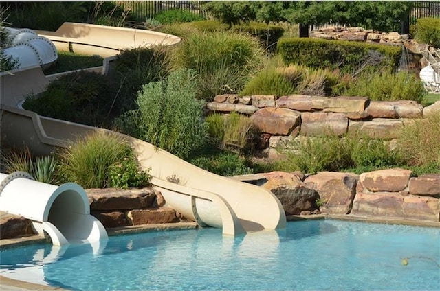 outdoor pool featuring a water slide and fence