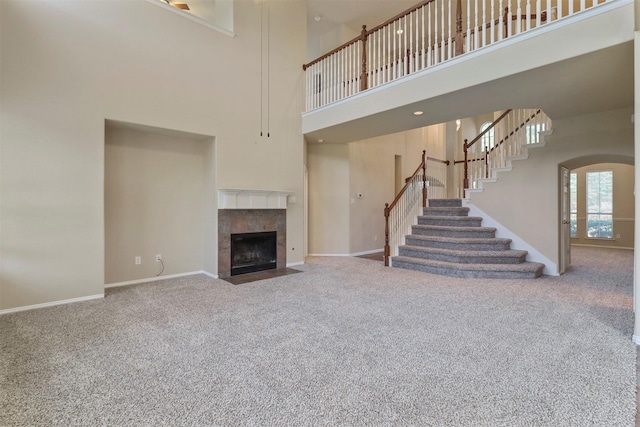 unfurnished living room with baseboards, carpet flooring, a high ceiling, and a fireplace