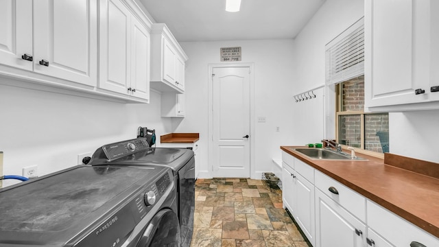 clothes washing area featuring cabinet space, stone finish flooring, washing machine and dryer, and a sink