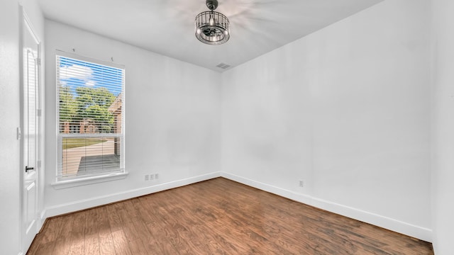 empty room featuring dark wood-type flooring, visible vents, and baseboards