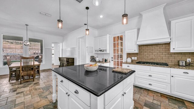 kitchen featuring custom exhaust hood, crown molding, stone tile flooring, a kitchen island, and backsplash