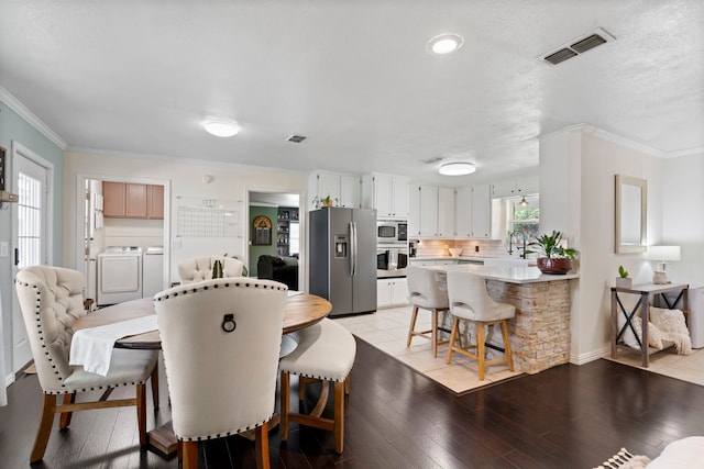 dining space featuring light wood-type flooring, visible vents, independent washer and dryer, and crown molding