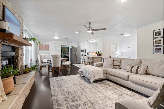 living room featuring ornamental molding, a stone fireplace, a ceiling fan, hardwood / wood-style flooring, and a textured ceiling