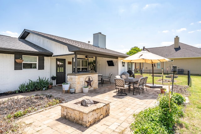 back of house featuring a shingled roof, a fire pit, fence, a patio, and brick siding
