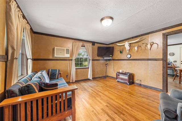 living room featuring baseboards, light wood-style floors, a textured ceiling, crown molding, and a wall unit AC