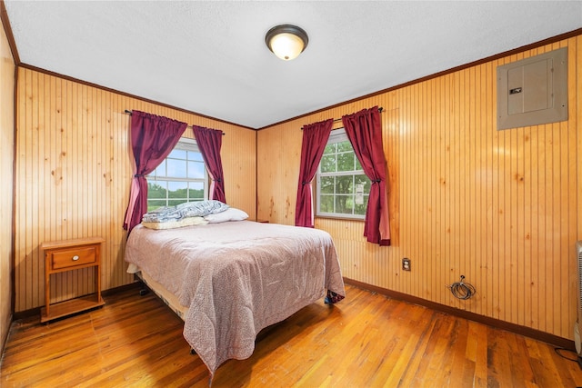 bedroom featuring electric panel, baseboards, hardwood / wood-style floors, and crown molding