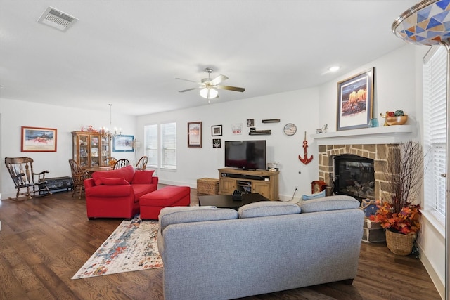 living area with visible vents, dark wood-type flooring, baseboards, a fireplace, and ceiling fan with notable chandelier
