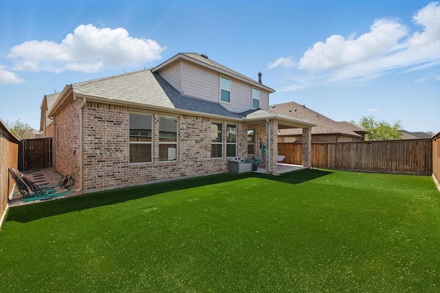 rear view of house with a fenced backyard, roof with shingles, a patio area, a lawn, and brick siding