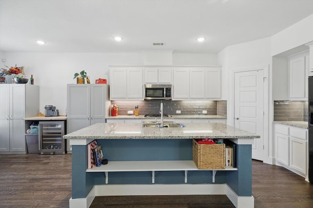 kitchen featuring wine cooler, a sink, stainless steel microwave, decorative backsplash, and open shelves