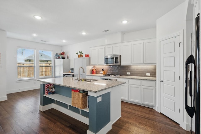 kitchen with stainless steel appliances, a sink, a center island with sink, decorative backsplash, and open shelves